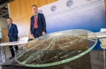 Two men in suits standing beside a shattered pane of glass.