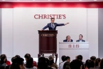 Salesroom with an auctioneer at a podium raising his hand over a crowd.