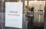 Sign reading 'MUSEUM CLOSED' in German posted to a glass door.