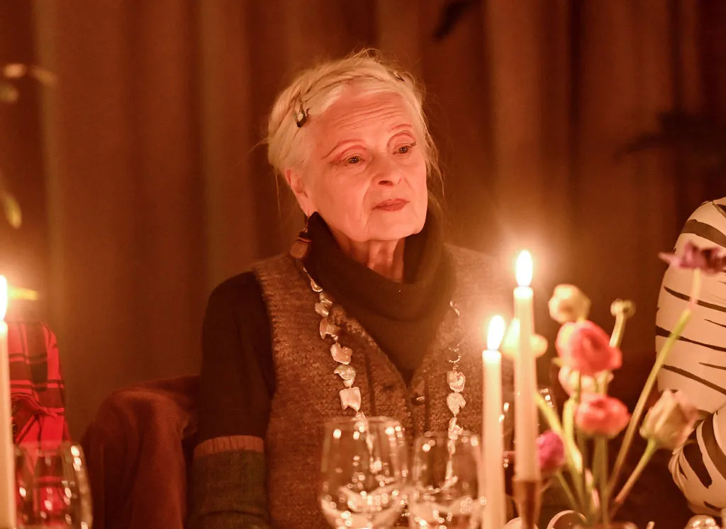 An woman in black turtleneck sits at a dinner table with pink and white flowers and a few lit candles.