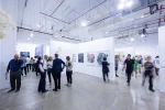 A long-exposure photograph showing people at the opening for an art exhibition. Several of the people are blurred.