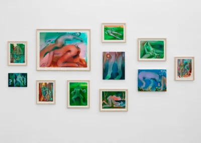 11 drawings of various sizes are hung on a white wall. They are in various unnatural colors like greens and reds showing human figures with elongated bodies. 