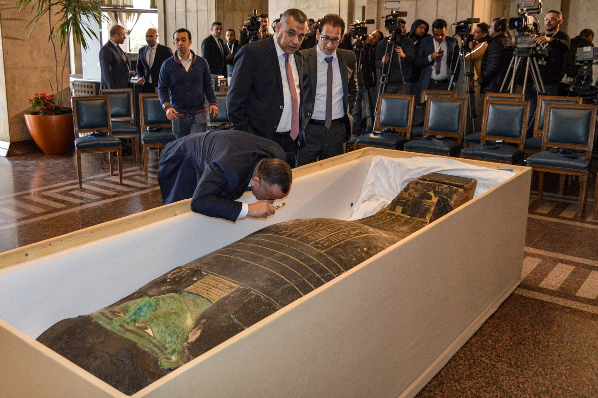 Man in a suit bends over a sarcophagus in a box.
