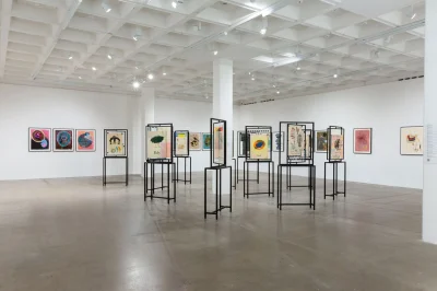 Installation view of a museum showing various abstract drawings. About half are installed on the walls, and the other half are installed in the center of the room on structures that show the front and back.