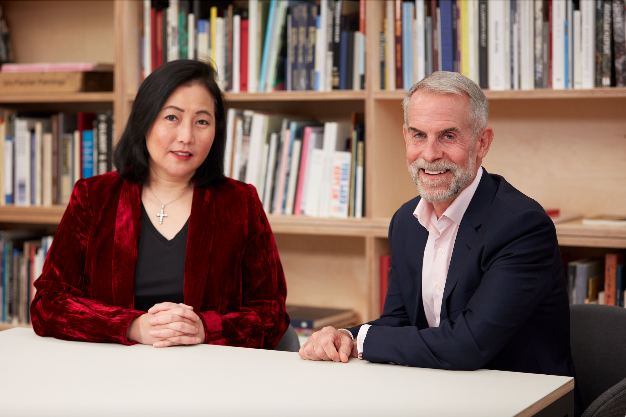 Man and woman sitting at table in front of book case.