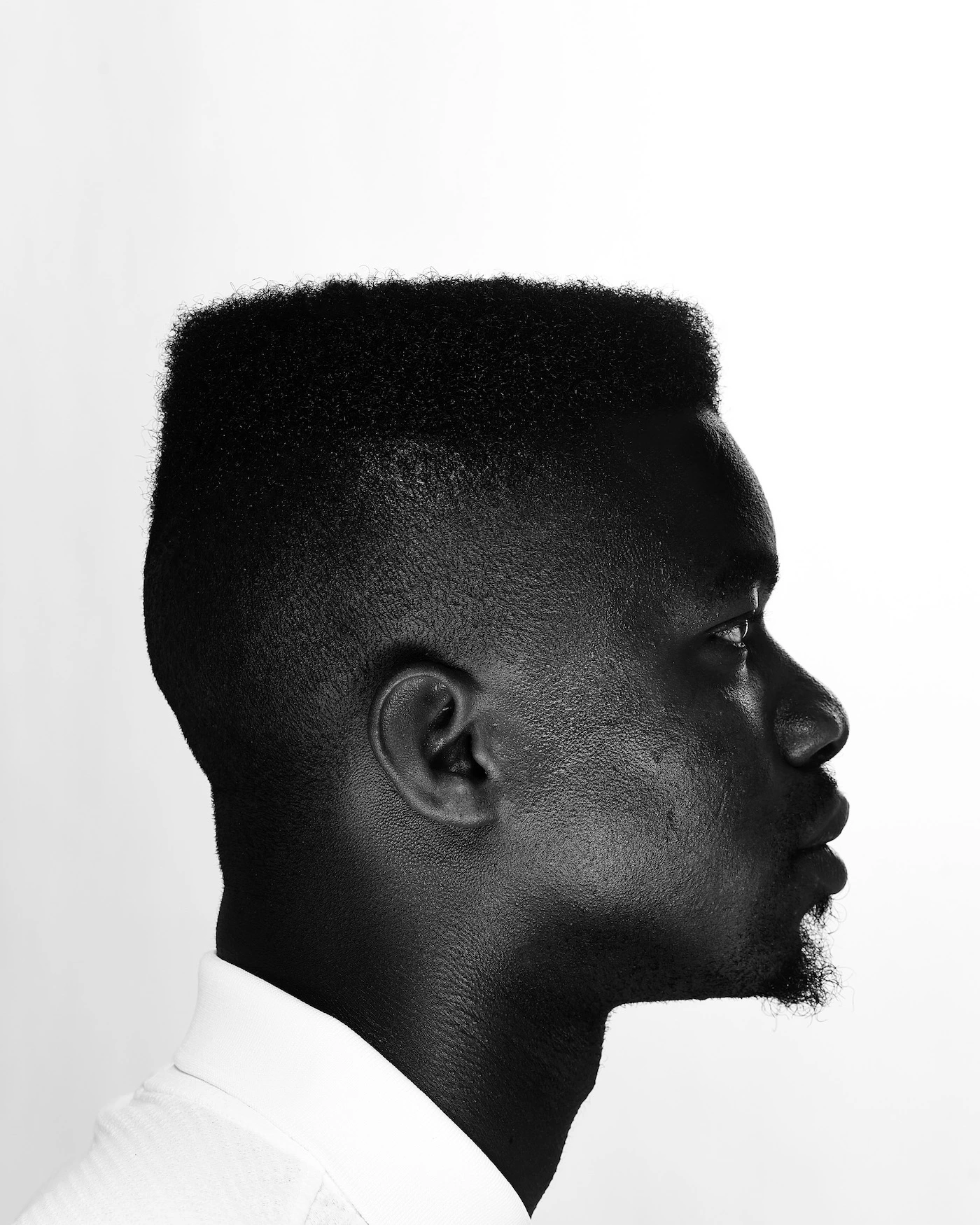 A Black man is shown in side profile with flat-top haircut against a white background.