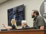 Two men and a women behind a podium at an auction for firearms.