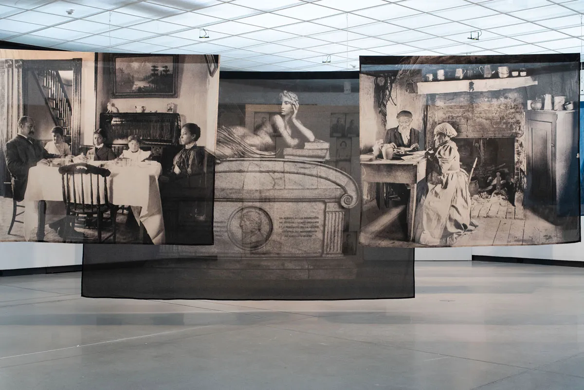 Installation view of three photographs printed on fabric that hang from the museum ceiling and overlap each other.