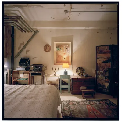A tattered loft room with a bed, a typewriter, candlesticks, and other objects.