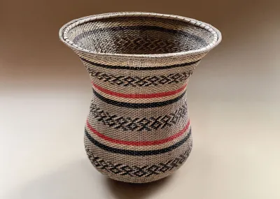A woven basked with stripes of red, white and black as well as a fish-like pattern in black.