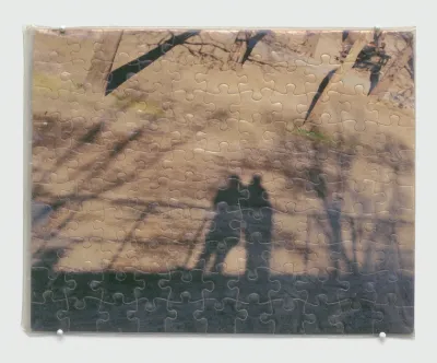 A completed puzzle of a photograph of the shadows of two figures staring at a sandy road.