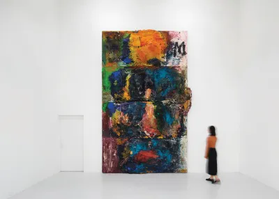 A person looks at a towering abstract painting with various layers built up.