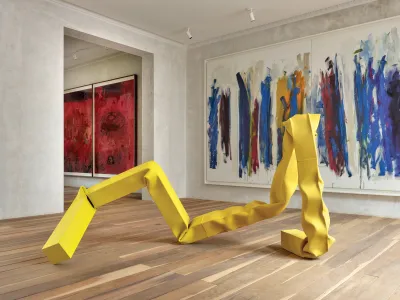 A sculpture of yellow twisted metal in front of two abstract paintings.