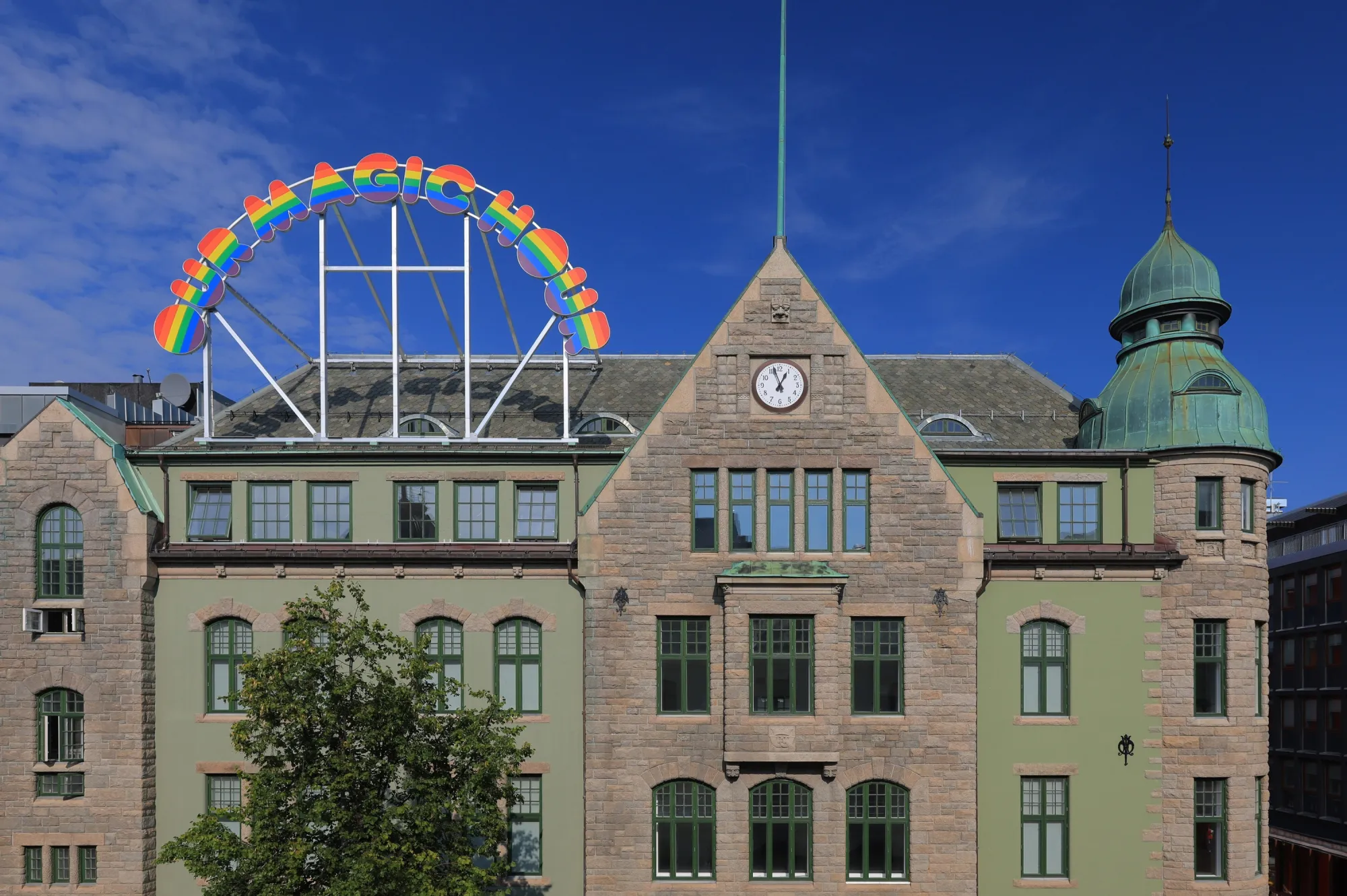 A building with a sign on the roof in the shape and colors of the rainbow.