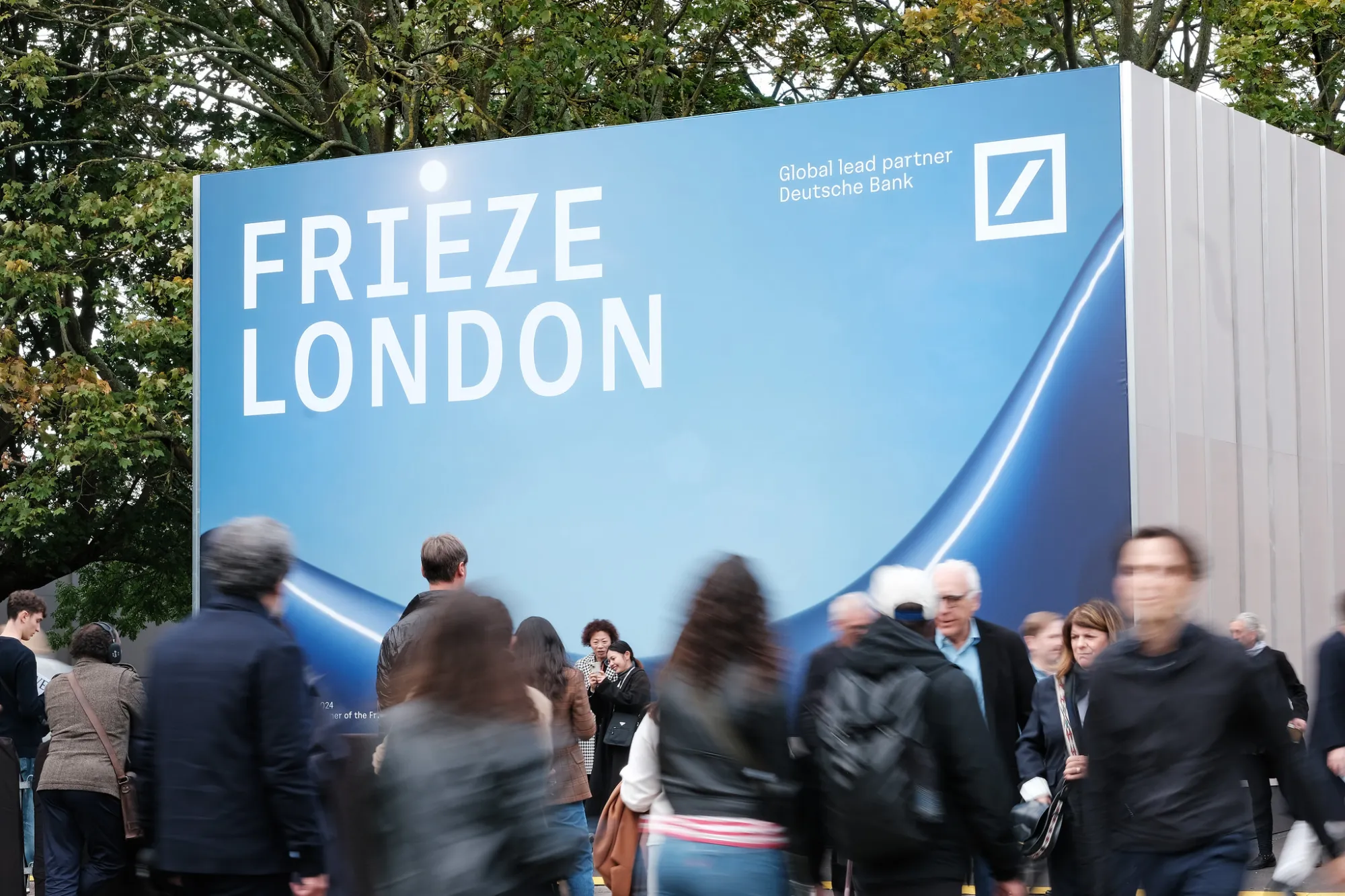 Fairgoers walk in front of the sign for Frieze London.