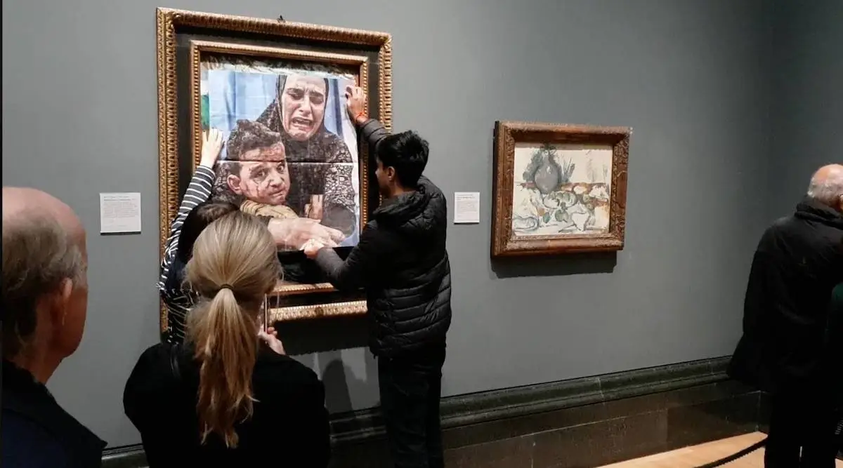 Two people pasting an image of a crying mother and child over a painting in a gallery.