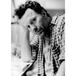 A white man in a plaid shirt holding his head with one hand.