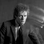 A white man in a suit with a blurred image of himself next to him.