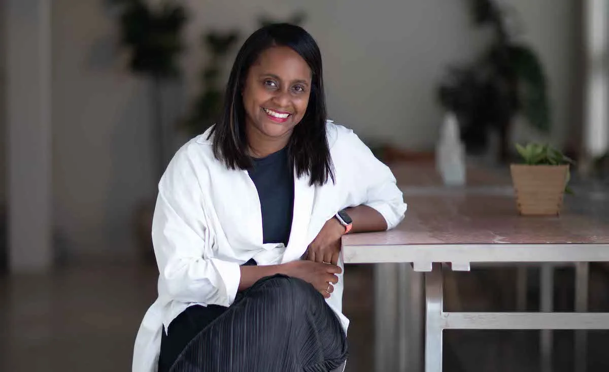 A Black woman smiling and sitting a table.