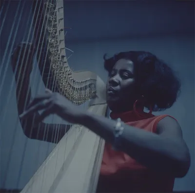 A Black woman strumming a harp.