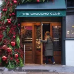 A woman in a coat walks through a door under a green awning.