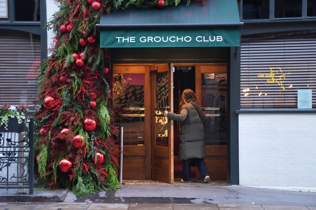 A woman in a coat walks through a door under a green awning.