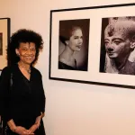 A Black woman standing beside a photograph showing a Black woman beside an ancient Egyptian sculpture.