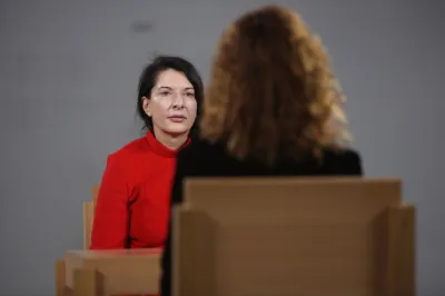 A woman in a red shirt seated at a table facing another woman.