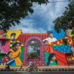 A building painted with a colorful mural of many different people interspersped with different patterns.