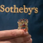 A hand holds a large golden ring studded with jewels.
