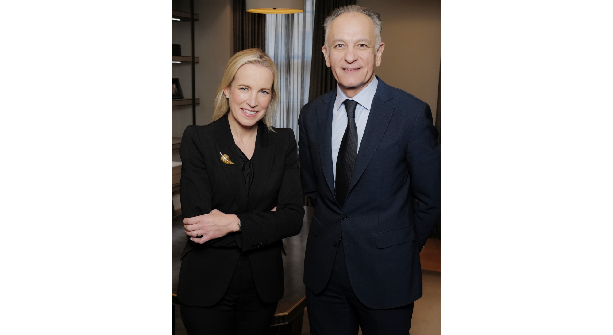 A blonde woman in black, left, stands next to a older gentleman in a suit.