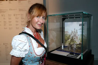 A woman in a frilly dress smiling before a glass case holding several watches.