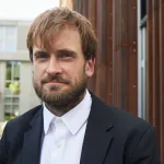A man with a beard and brown hair smiles at the camera.