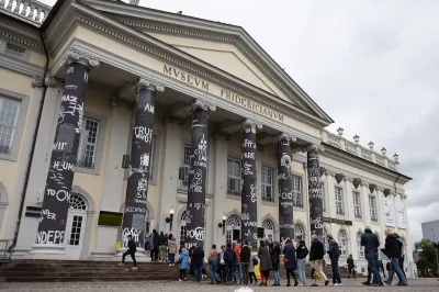 A line of people walking into a museum with banners surroundings its columns.