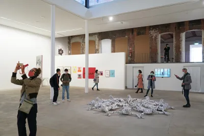 Masked people taking pictures of art on their phones in a gallery.