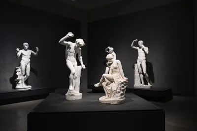 Several ancient sculptures of nude men and women in a darkened room.
