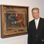 A man in a suit beside a painting of a smoking pipe and hands.