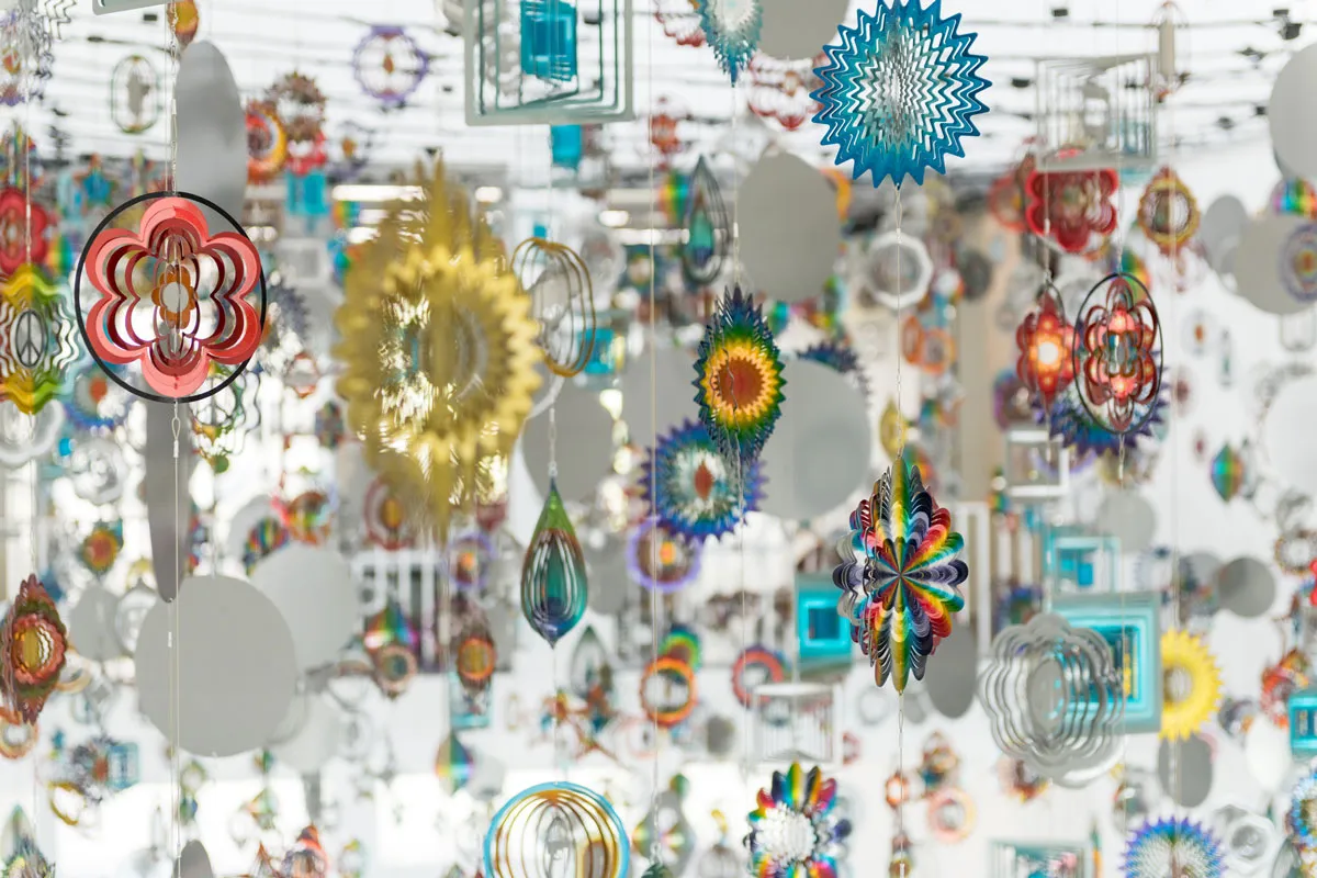 Detail of a hanging installation of various brightly colored wind spinners that variously show tears, guns, bullets at their centers.
