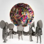 Five soundsuits in silver are all connected to each other with the heads appearing like megaphones. Above is a circular abstraction of brightly colored fur.