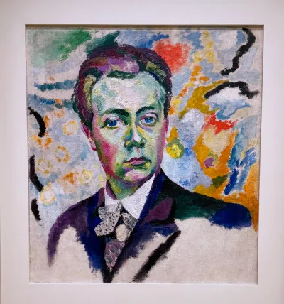 A colorful self-portrait of an artist wearing a suit. The bottom of the painting is left unfinished.