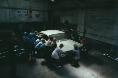 A bunch of people are squatting around a vintage cadillac in a garage.