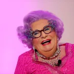 A smiling man in a pink wig and dress.