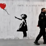 A man walks past a mural of a girl in a dress on a wall.