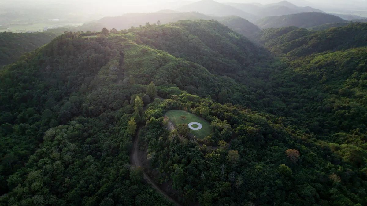 An aerial view of a lush Thai landscape with rolling hills. IN the center is a circular Land art installation.
