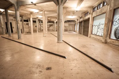 Two long metal bars are installed in a former warehouse with graffiti on its exterior windows.