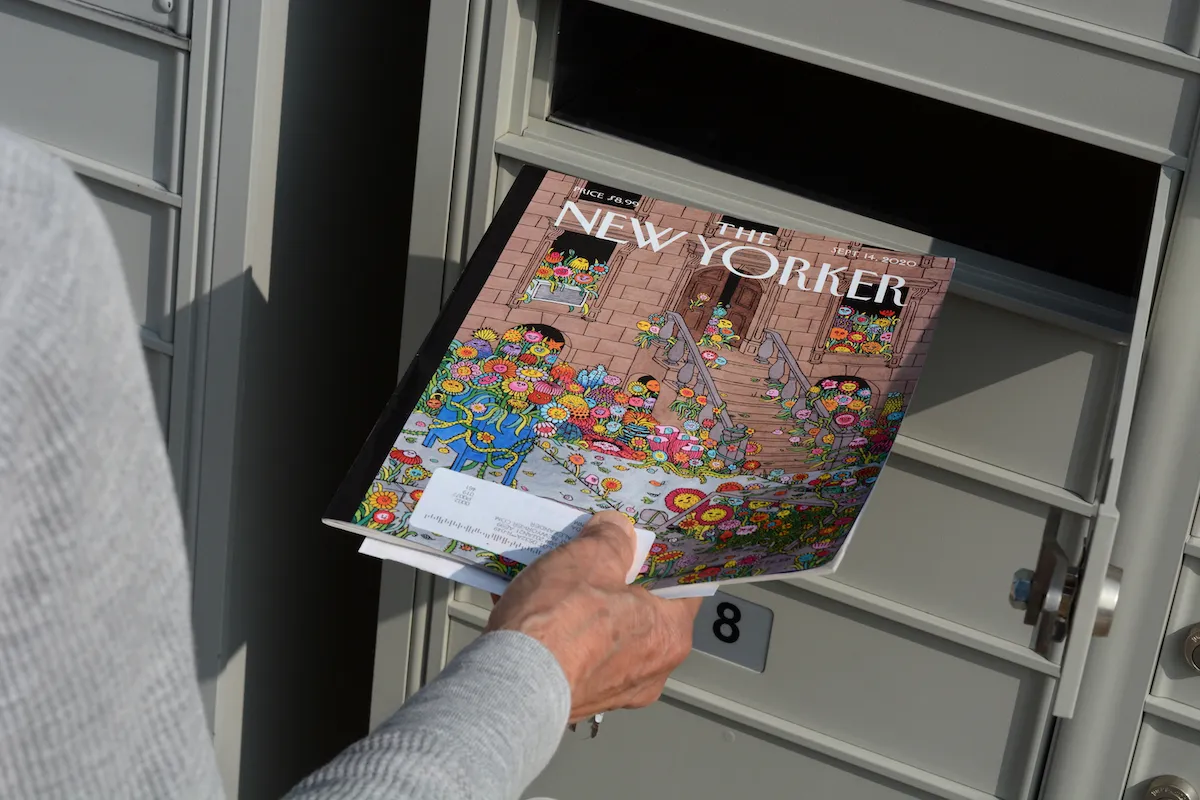 A person placing a print edition of the New Yorker magazine into a mailbox.