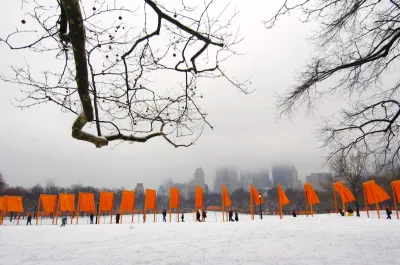 A series of a saffron-colored portals with flowing fabric hanging down, along with people walking below in the snow.
