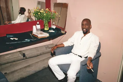 A Black man in a chair smoking a cigarette.