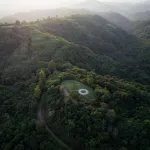 An aerial view of a lush Thai landscape with rolling hills. IN the center is a circular Land art installation.