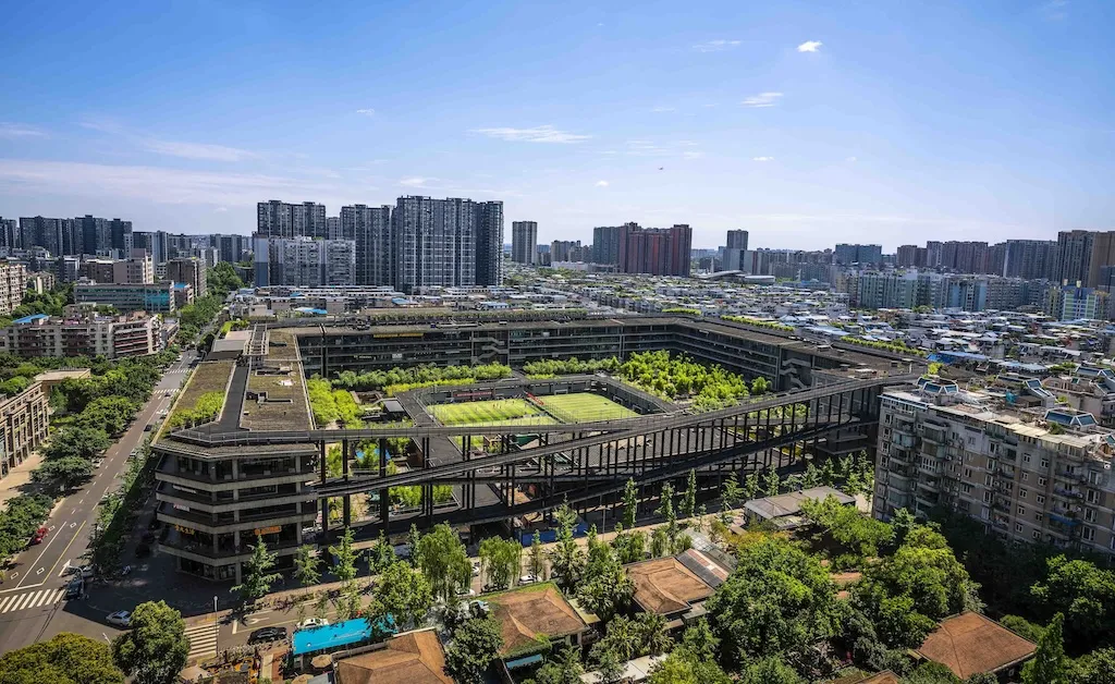 A five-story mixed-use complex with walkways and ramps connecting open-air plazas, shops, restaurants, and sports facilities